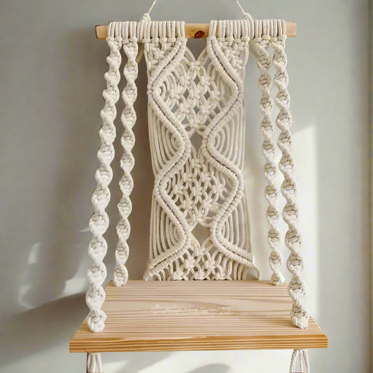 Macrame wall hanging with wooden base on a plain background